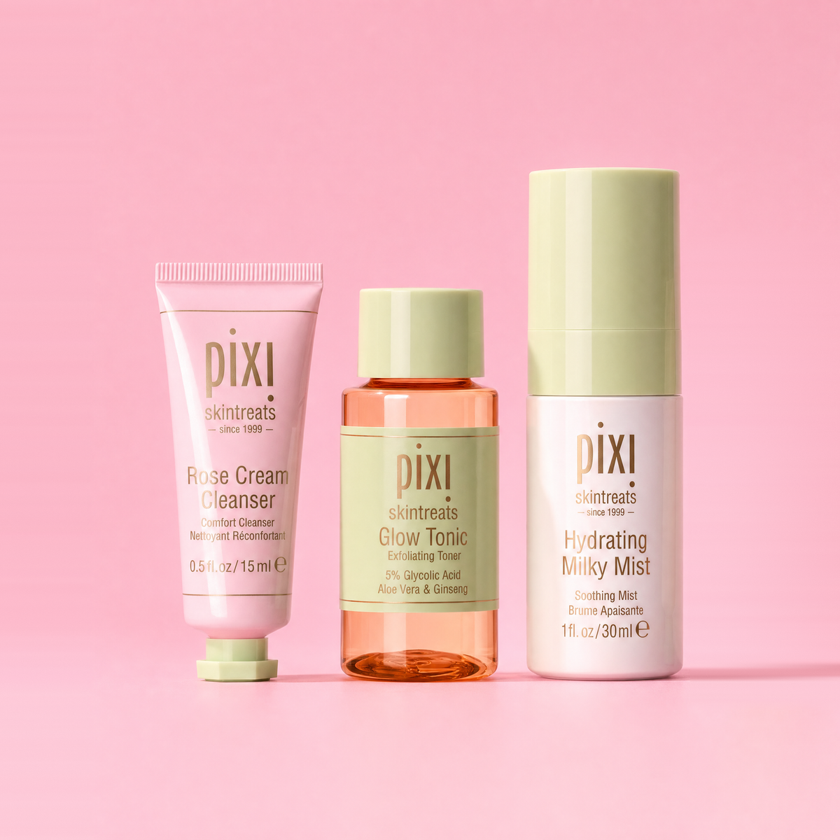 Three Pixi skincare products arranged on a solid pink background: a pink cleanser tube, an amber glow tonic bottle with a pale green cap, and a white hydrating mist bottle with a pale green cap. Visible brand text reads pixi skincare.