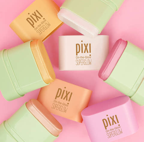 Pixi On-the-Glow SuperGlow cream products in pastel shades arranged in a circular flat-lay pattern on a solid pink background.