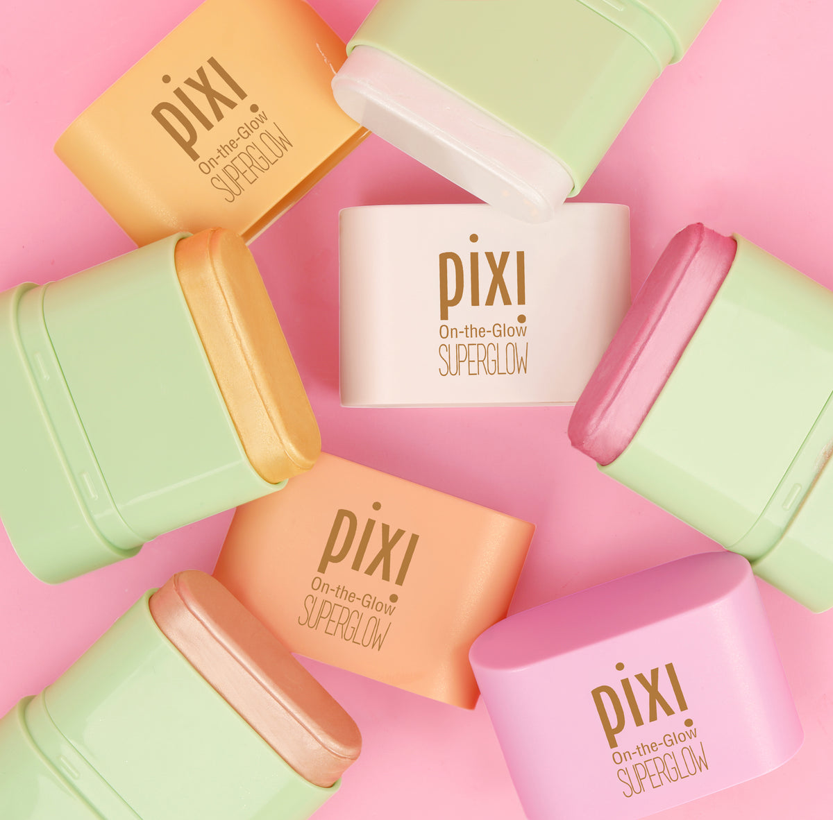 Pixi On-the-Glow SuperGlow cream products in pastel shades arranged in a circular flat-lay pattern on a solid pink background.