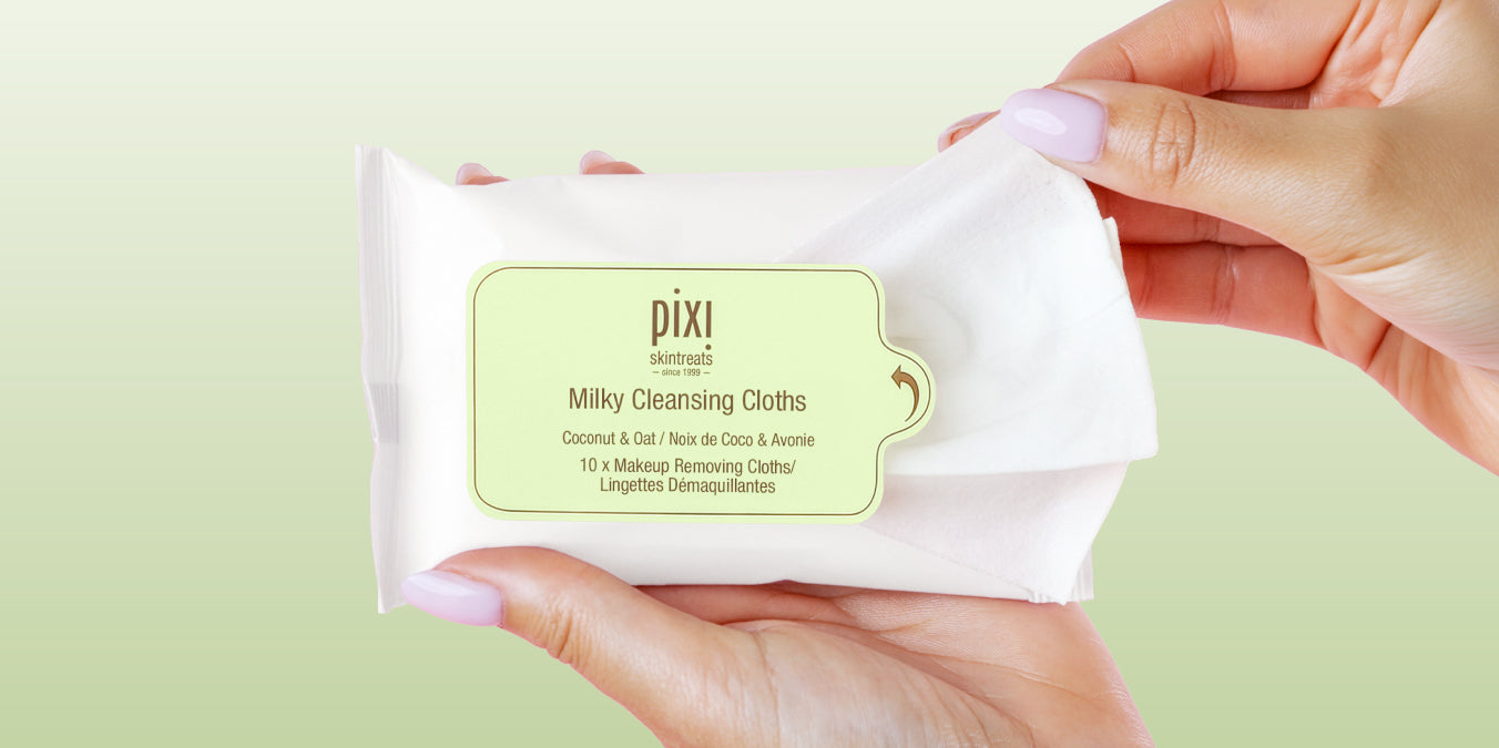 Milky Cleansing Cloths on a green background being opened with a hand