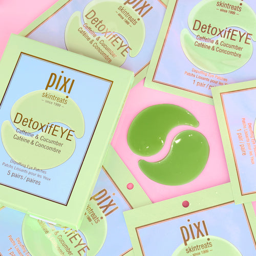 Several Pixi Skintreats DetoxiEYE caffeine and cucumber eye patches and their packaging are arranged on a pastel pink background. The packaging is light green and lavender, and one green patch is shown. view 2
