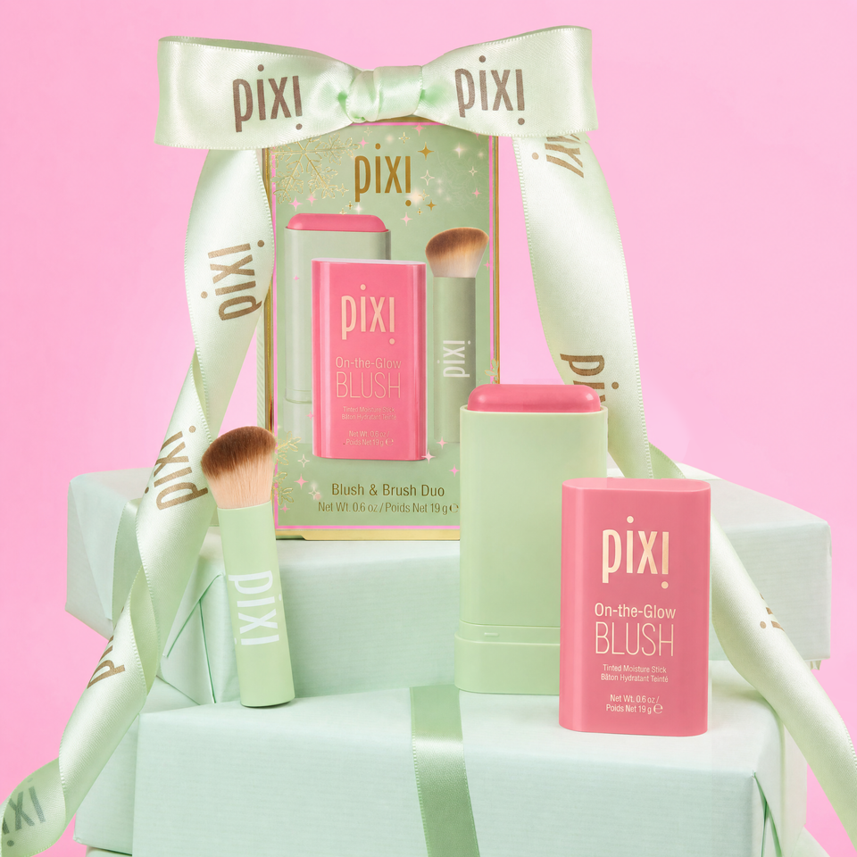 Pixi On-the-Glow BLUSH and Brush duo gift set with pastel green and pink packaging, wrapped in a mint green satin ribbon with the Pixi logo, set against a solid pink background. view 1